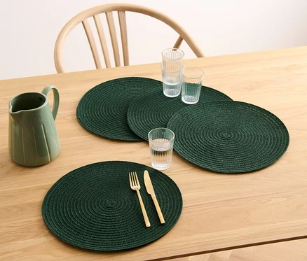 Sur une table en bois, il y a quatre sets de table ronds verts, un pichet et des verres.