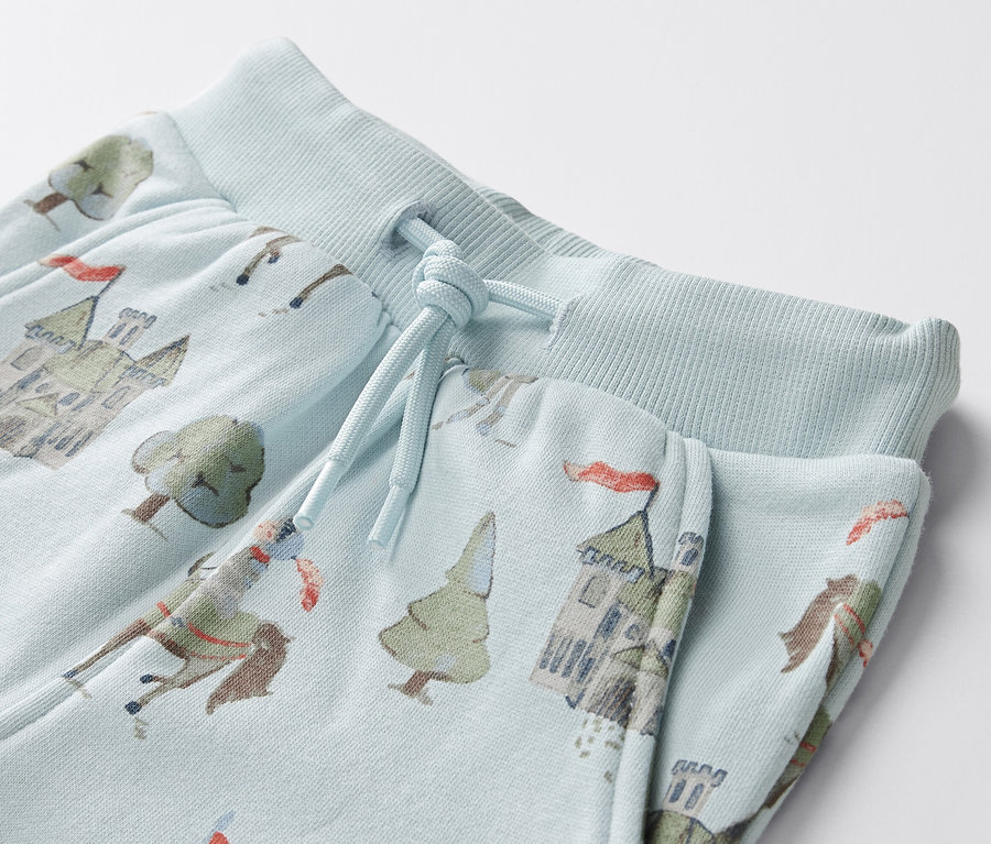 Gros plan sur un pantalon de survêtement bleu clair pour bébé, imprimé de chevaliers, de châteaux et d'arbres.