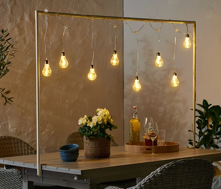 Une barre de table décorative avec guirlande lumineuse à LED illumine une table avec des fleurs, des boissons et des bols bleus.