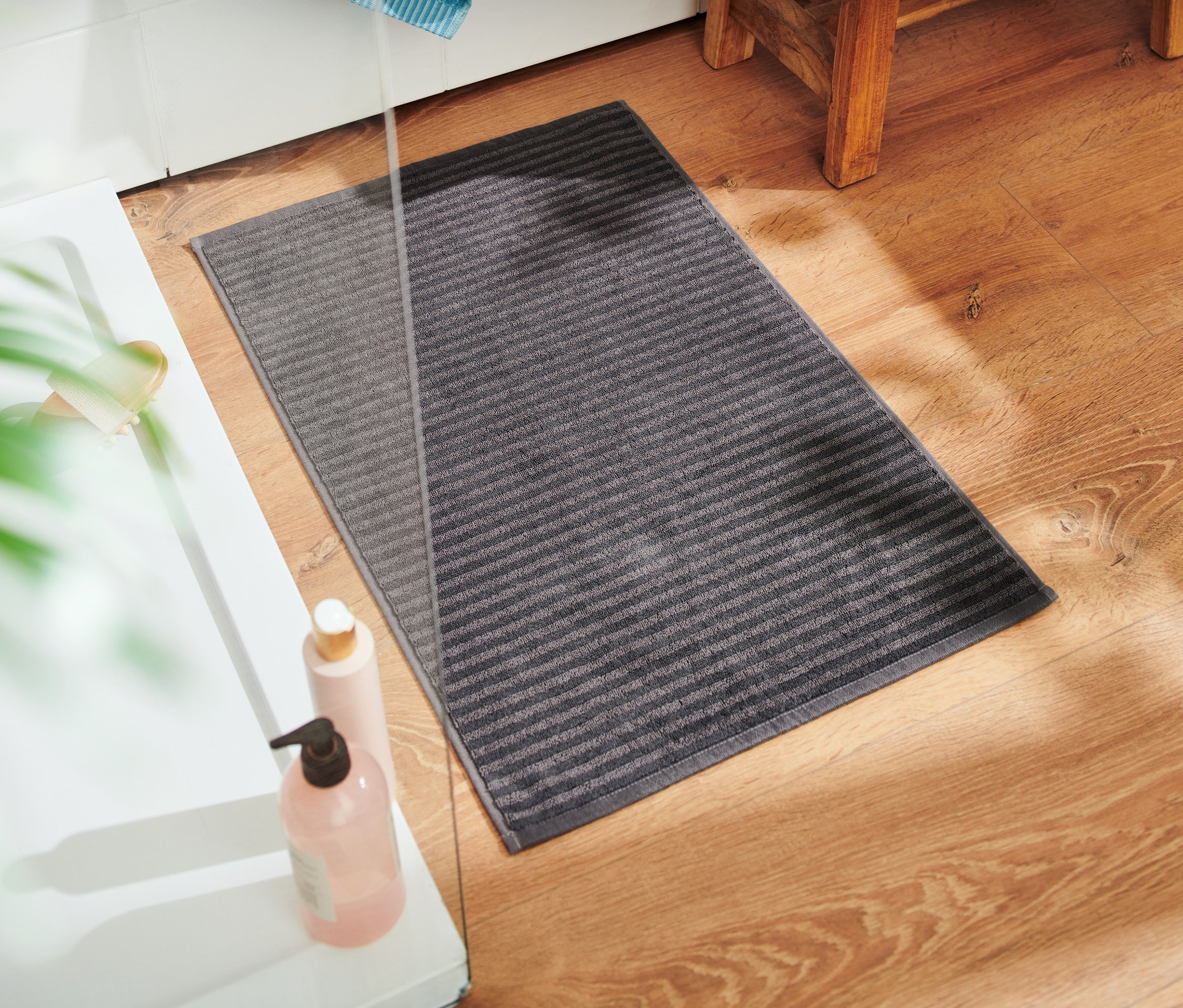 Un tapis de bain en éponge anthracite est posé sur un plancher en bois à côté d'une baignoire.