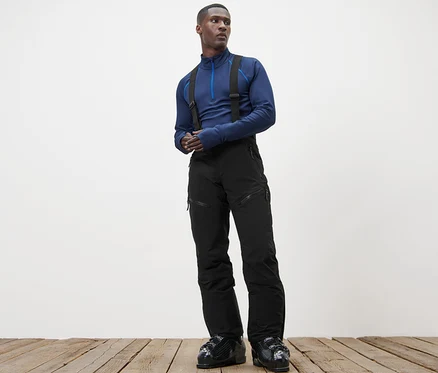 Un homme debout sur un plancher en bois porte un haut bleu et un pantalon de ski high-tech.