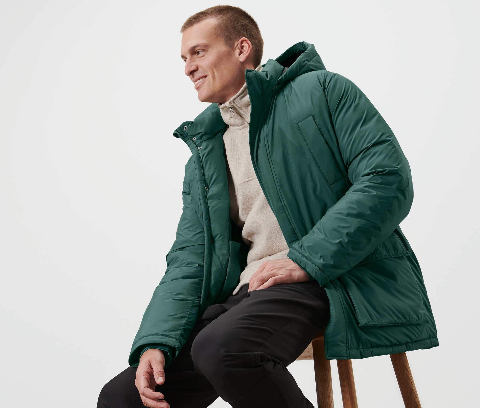 Un homme est assis sur un tabouret et porte une parka matelassée.