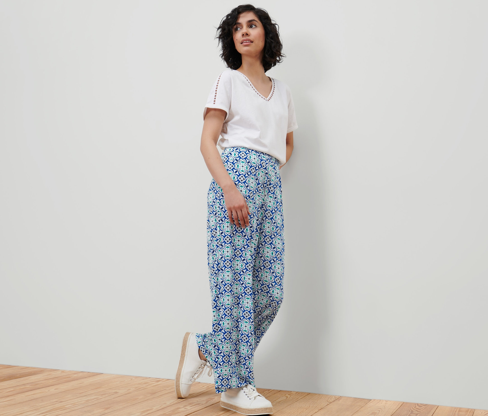 Une femme se tient debout contre un mur et porte un chemisier blanc et un pantalon palazzo à imprimé intégral.