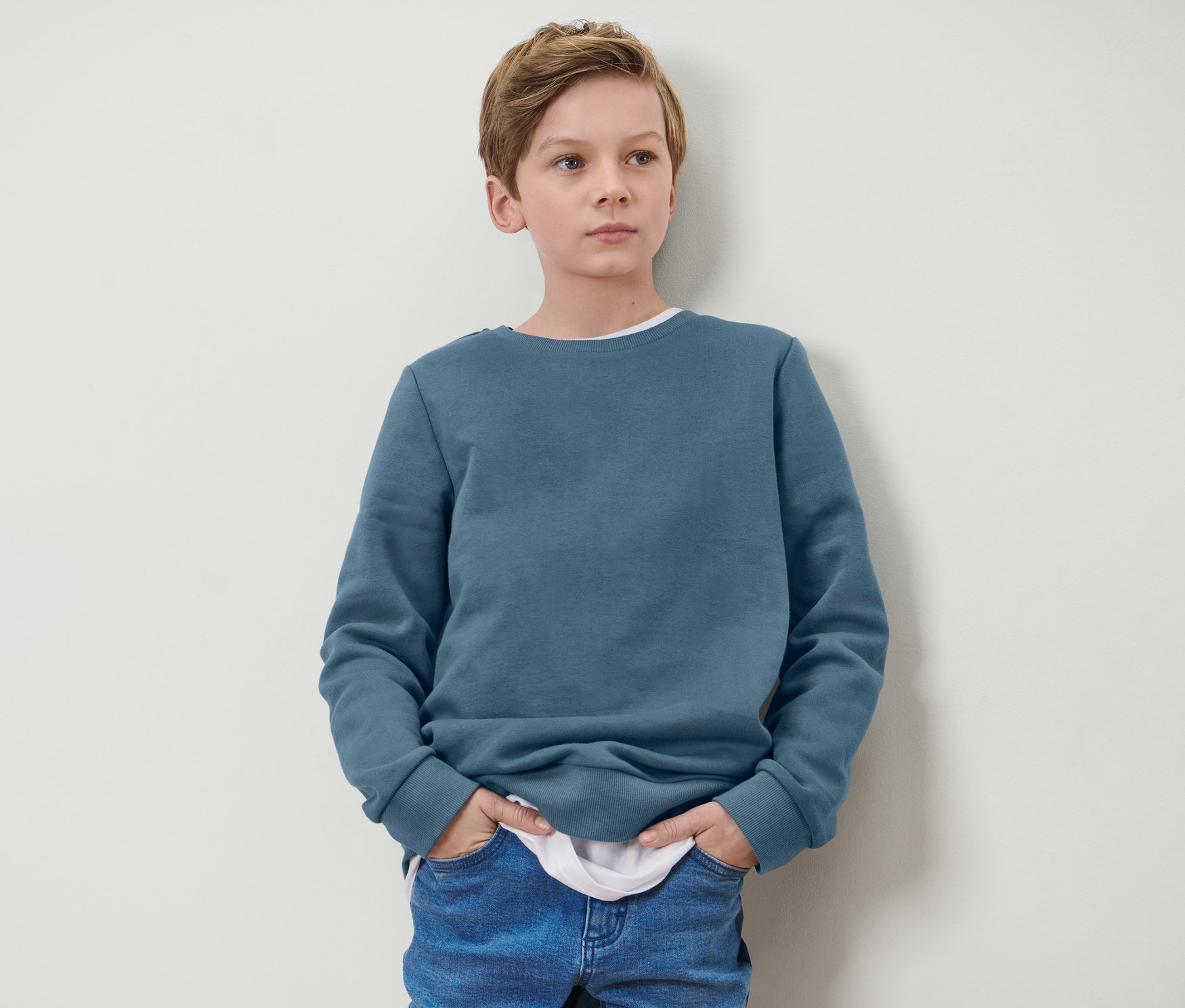Garçon debout, les mains dans les poches d'un sweat-shirt bleu pour enfant.