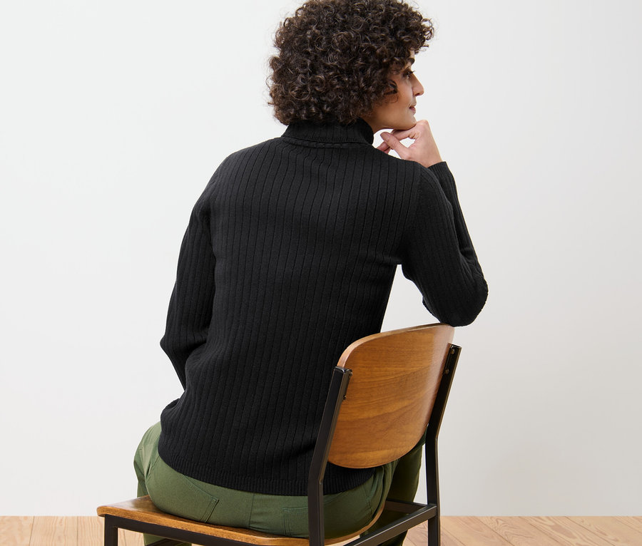 Une femme est assise sur une chaise et porte un pull à col roulé côtelé noir.