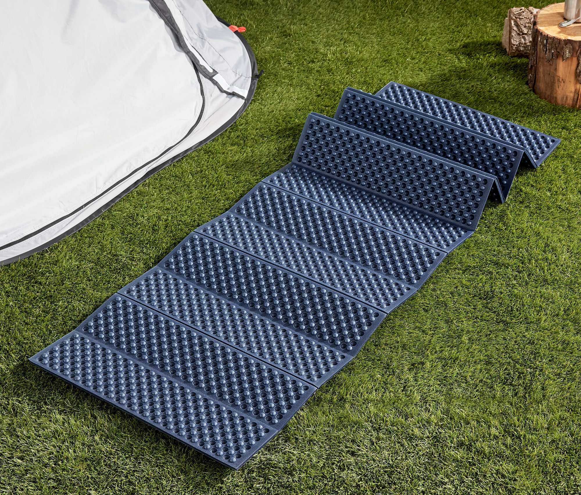 Un tapis isolant pliable bleu est posé sur l'herbe à côté d'une tente.