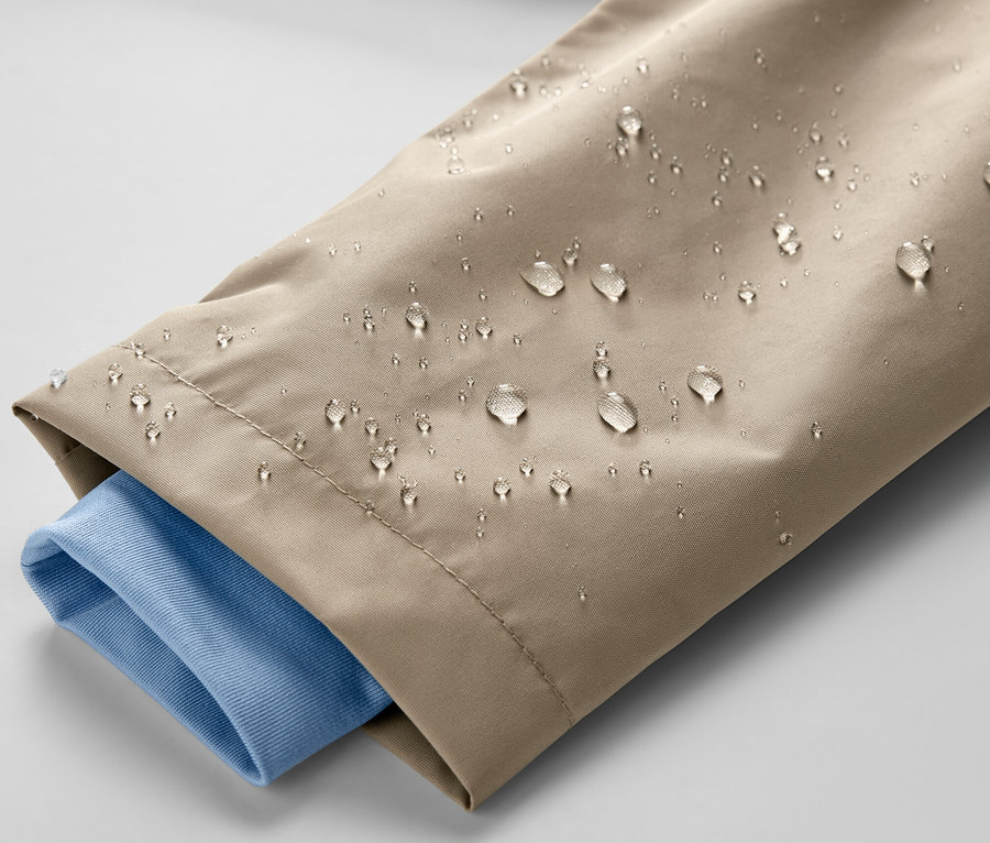 Gros plan sur une veste de pluie marron pour enfant, avec des gouttes d'eau et une manche de chemise bleue.