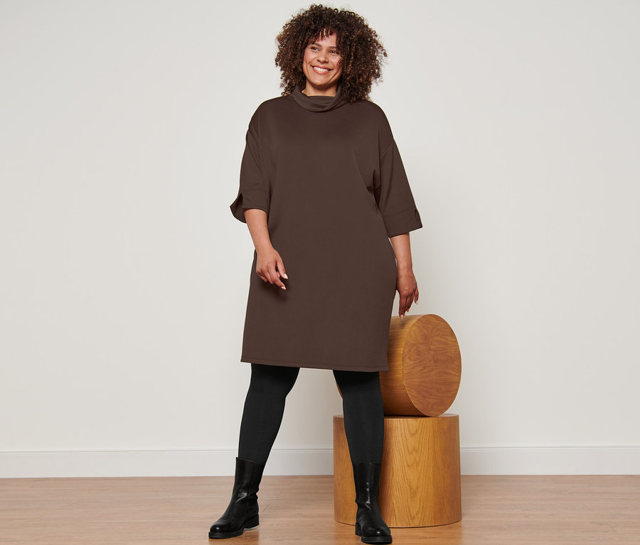 Femme posant en robe sweat, collants thermiques noirs et bottines en cuir.