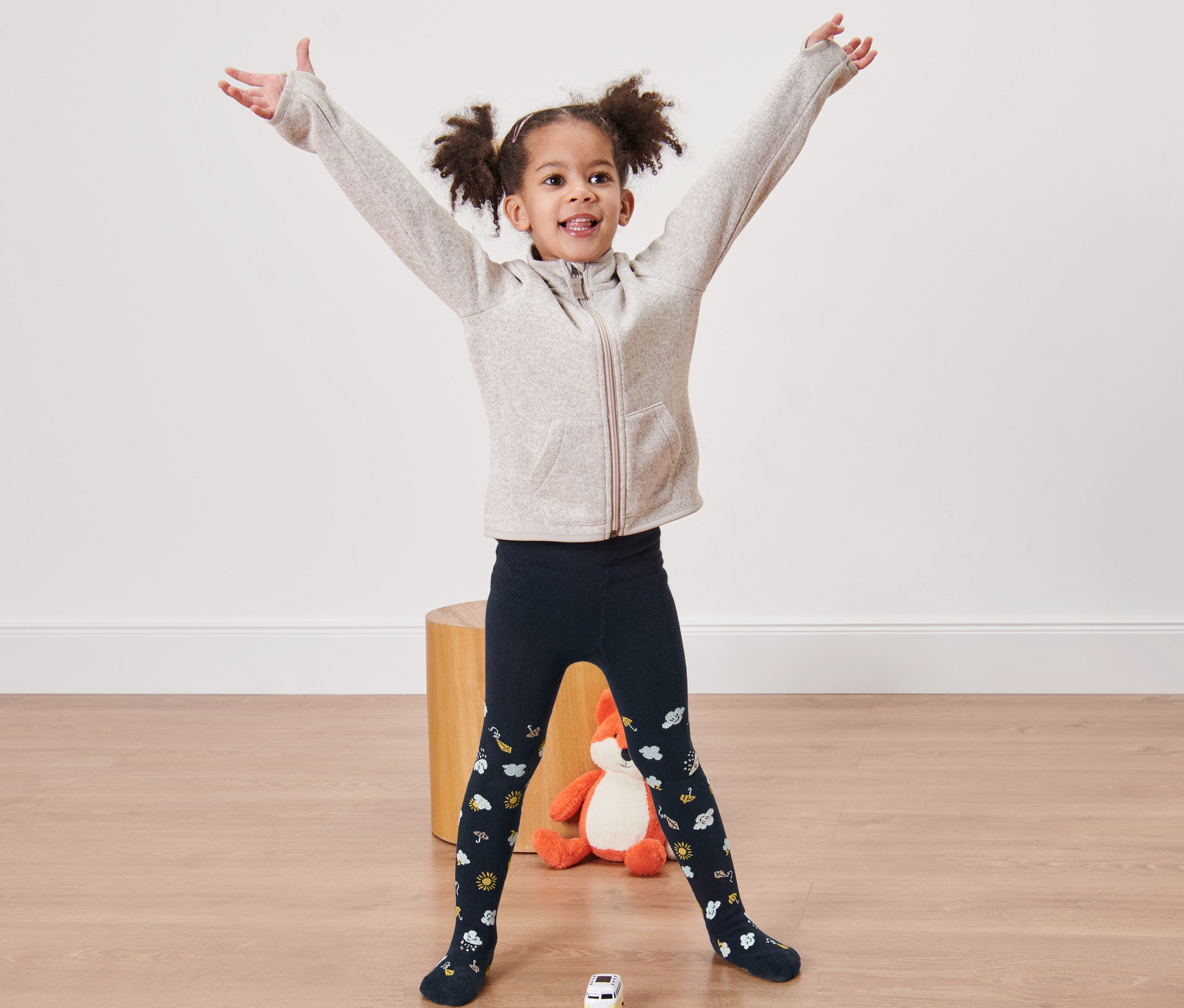 Une fillette souriante se tient debout, les bras écartés, et porte des collants bleus.