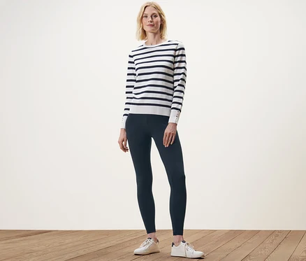 Une femme pose debout en legging bleu marine et pull rayé.