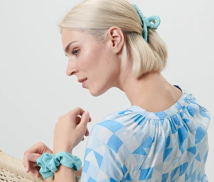 Une femme blonde est assise dans un fauteuil, portant un élastique à cheveux au poignet et une pince à cheveux. Ensemble d'accessoires à cheveux.
