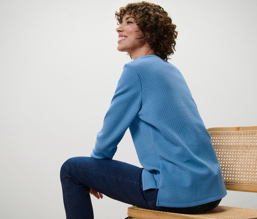 Une femme est assise sur une chaise et porte un sweat-shirt structuré bleu clair.