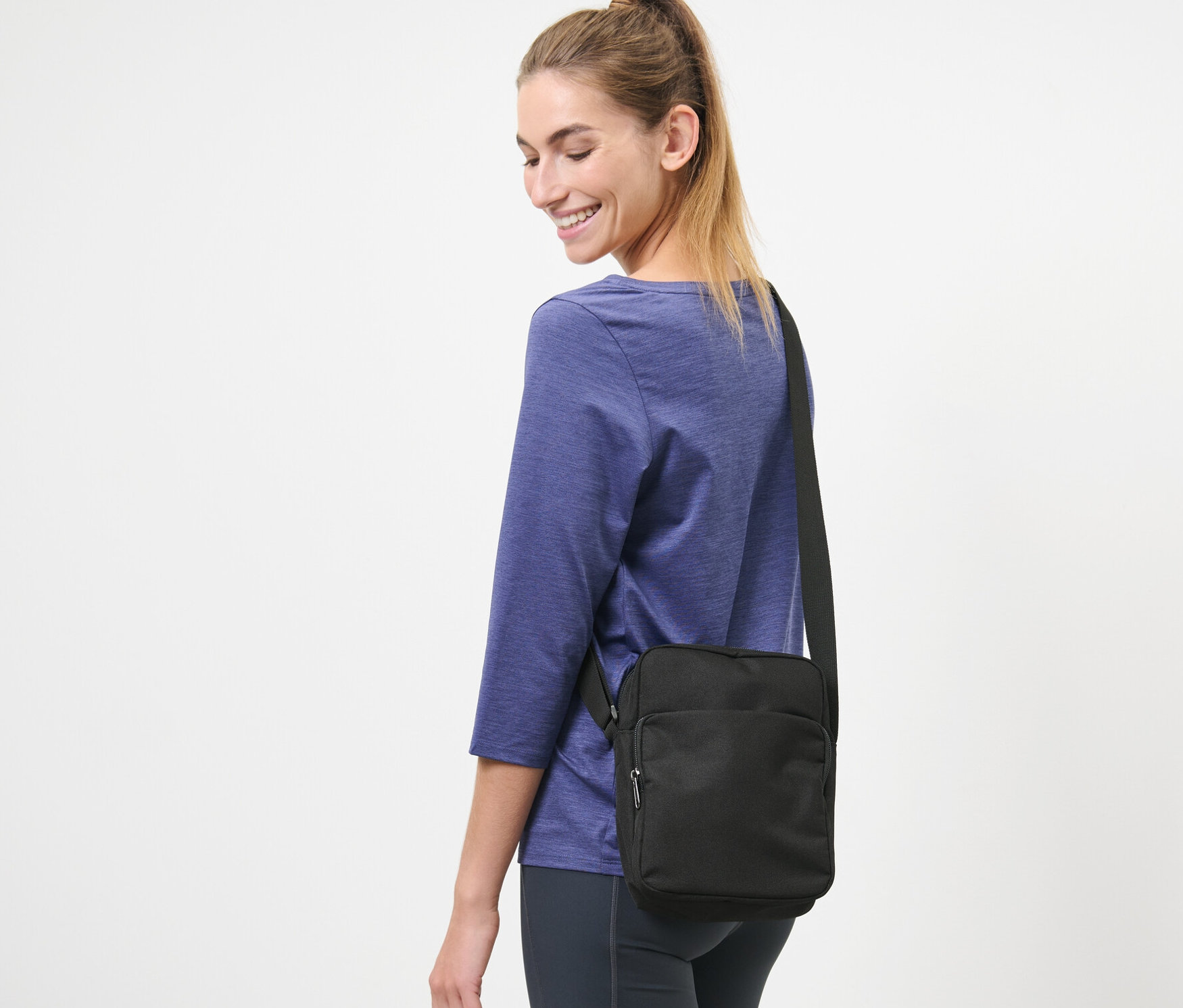 Femme souriante avec un sac bandoulière noir.