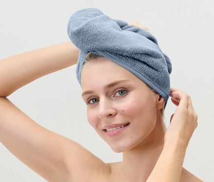 Femme ajustant une serviette turban bleu clair sur sa tête.