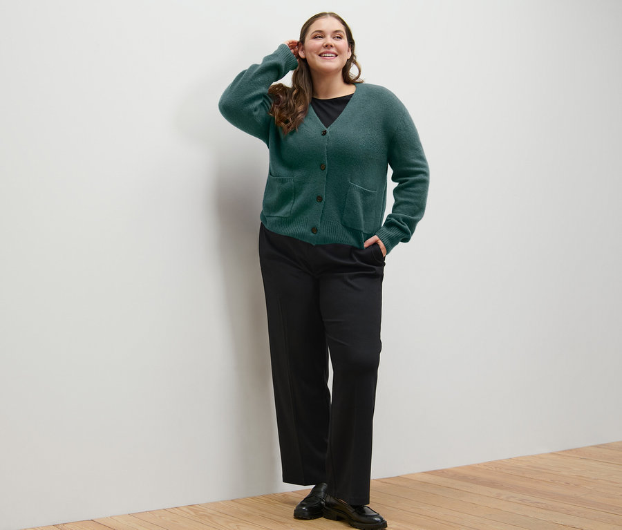 Femme posant en jaquette en maille vert foncé avec de la laine et pantalon en jersey confortable.