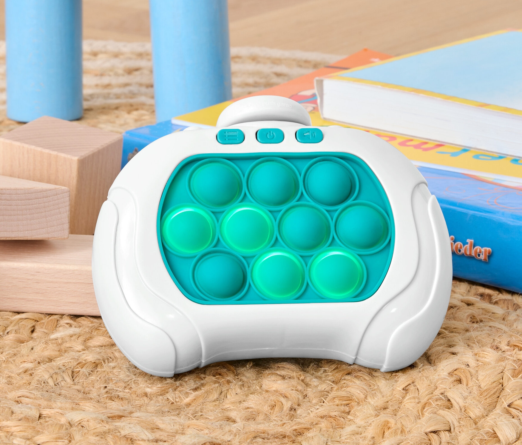 Un jeu Pop-It est posé sur un tapis entre des blocs de bois et des livres.