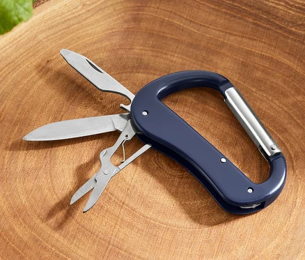 Un mousqueton avec outils polyvalents 5 en 1 avec couteau, scie et ciseaux posé sur une souche d'arbre.