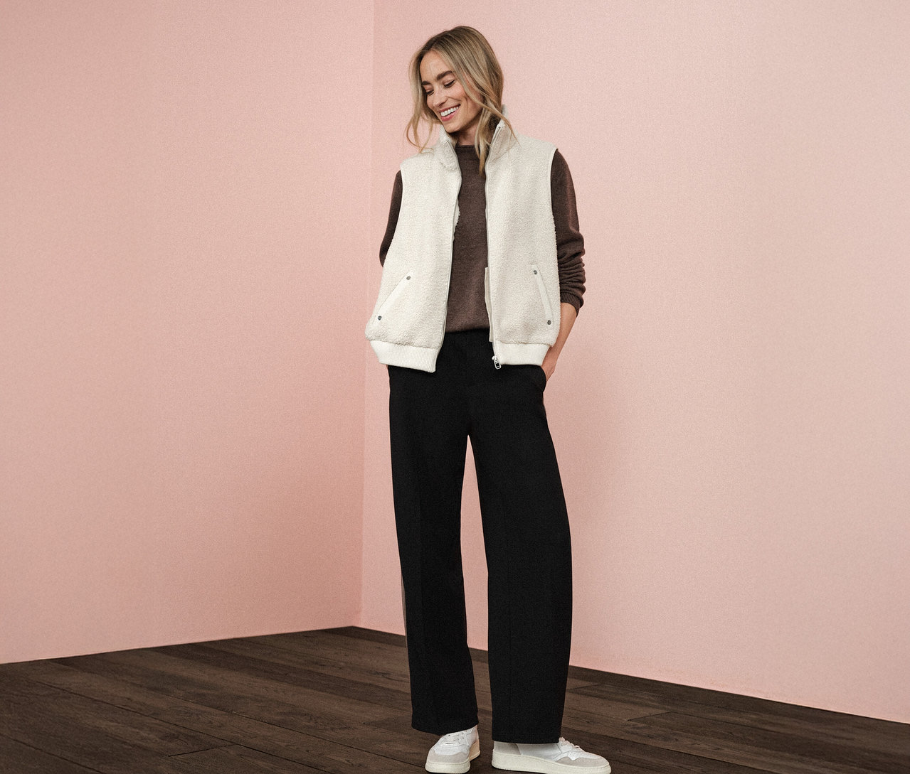 Une femme porte une veste en teddy Street One sur un pull marron, associé à un pantalon noir et des baskets blanches.