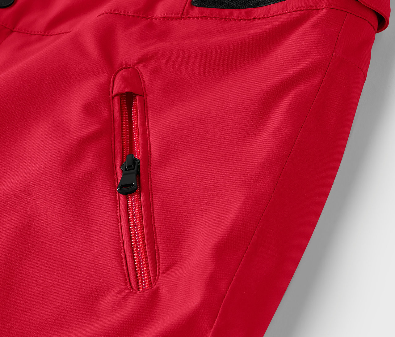 Détail d'une veste rouge avec une fermeture éclair noire sur la poche.