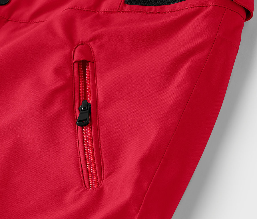 Détail d'une veste rouge avec une fermeture éclair noire sur la poche.