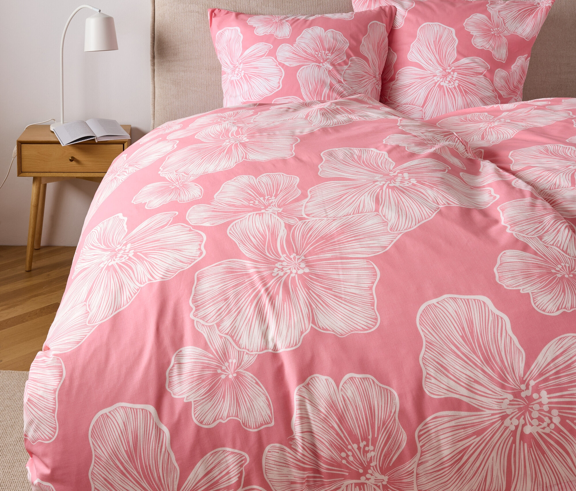 Gros plan d'un lit avec une literie en polycoton rose à motifs floraux blancs, comprenant des coussins de taille standard et de grande taille.