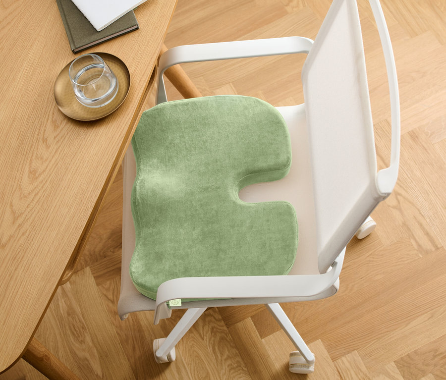 Coussin de siège vert avec une découpe en forme de U sur une chaise. La chaise est placée près d'une table en bois.