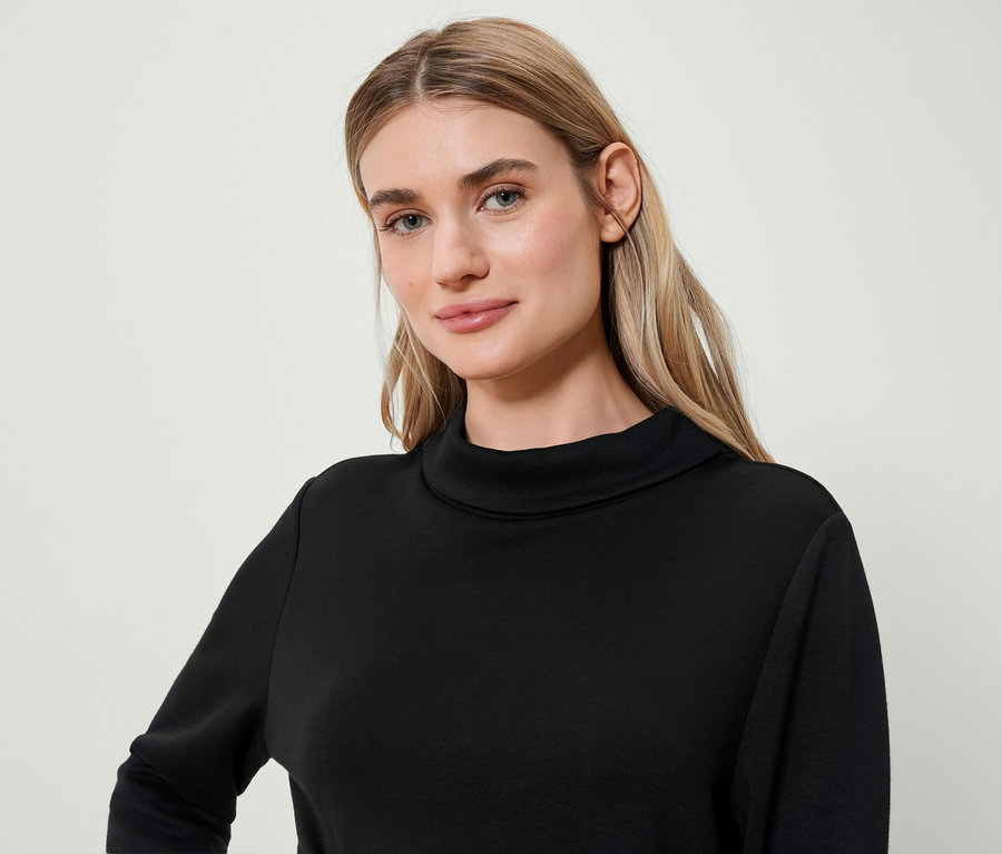 Portrait d'une femme blonde portant un pull à col roulé noir.