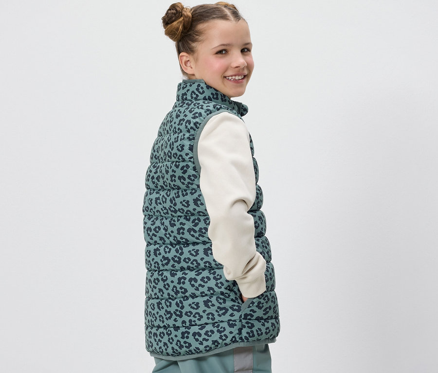 Une fille souriant par-dessus son épaule porte une veste matelassée Kinder avec un imprimé léopard.