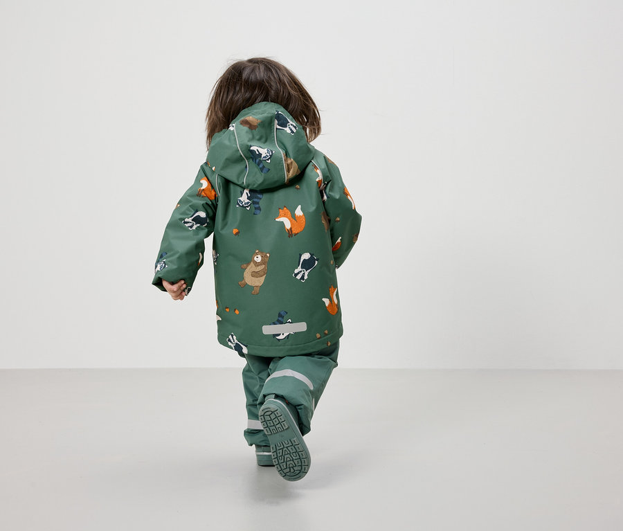 Un jeune enfant vu de dos marche dans une veste et un pantalon verts à motifs d'animaux.