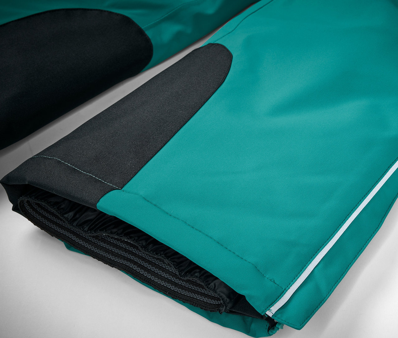 Gros plan sur un pantalon de ski vert émeraude avec des détails noirs et une bande blanche.