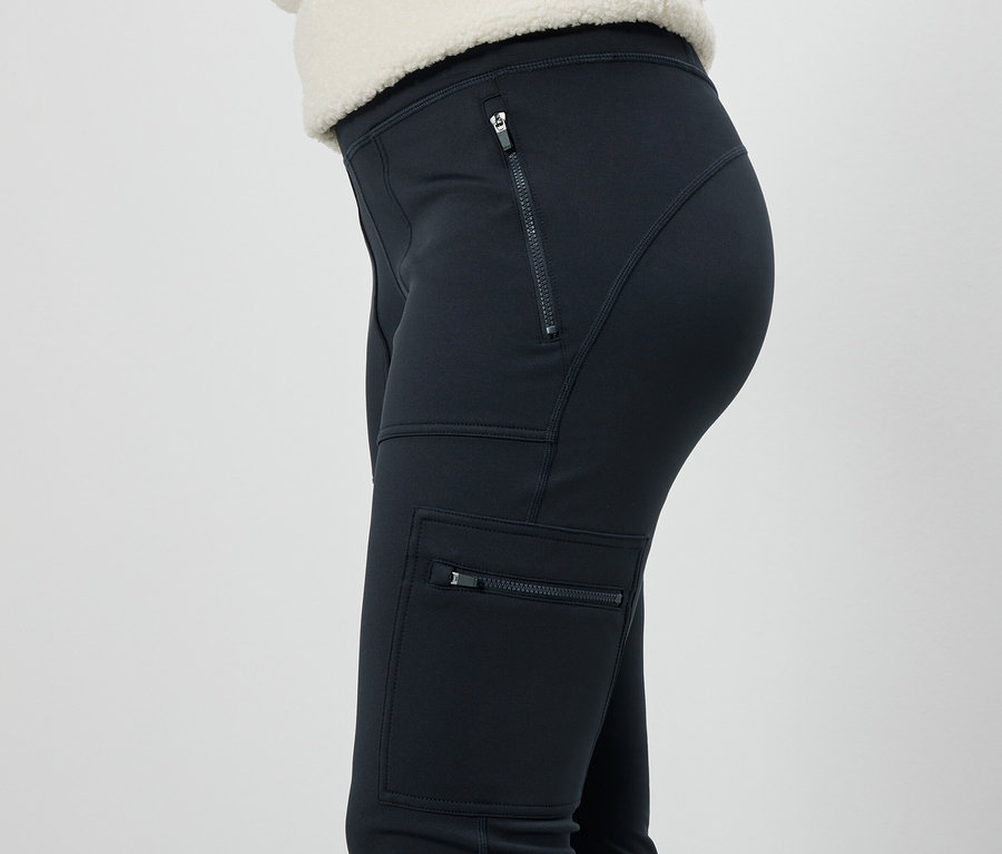 Vue latérale d'une femme portant un pantalon noir avec des poches zippées.