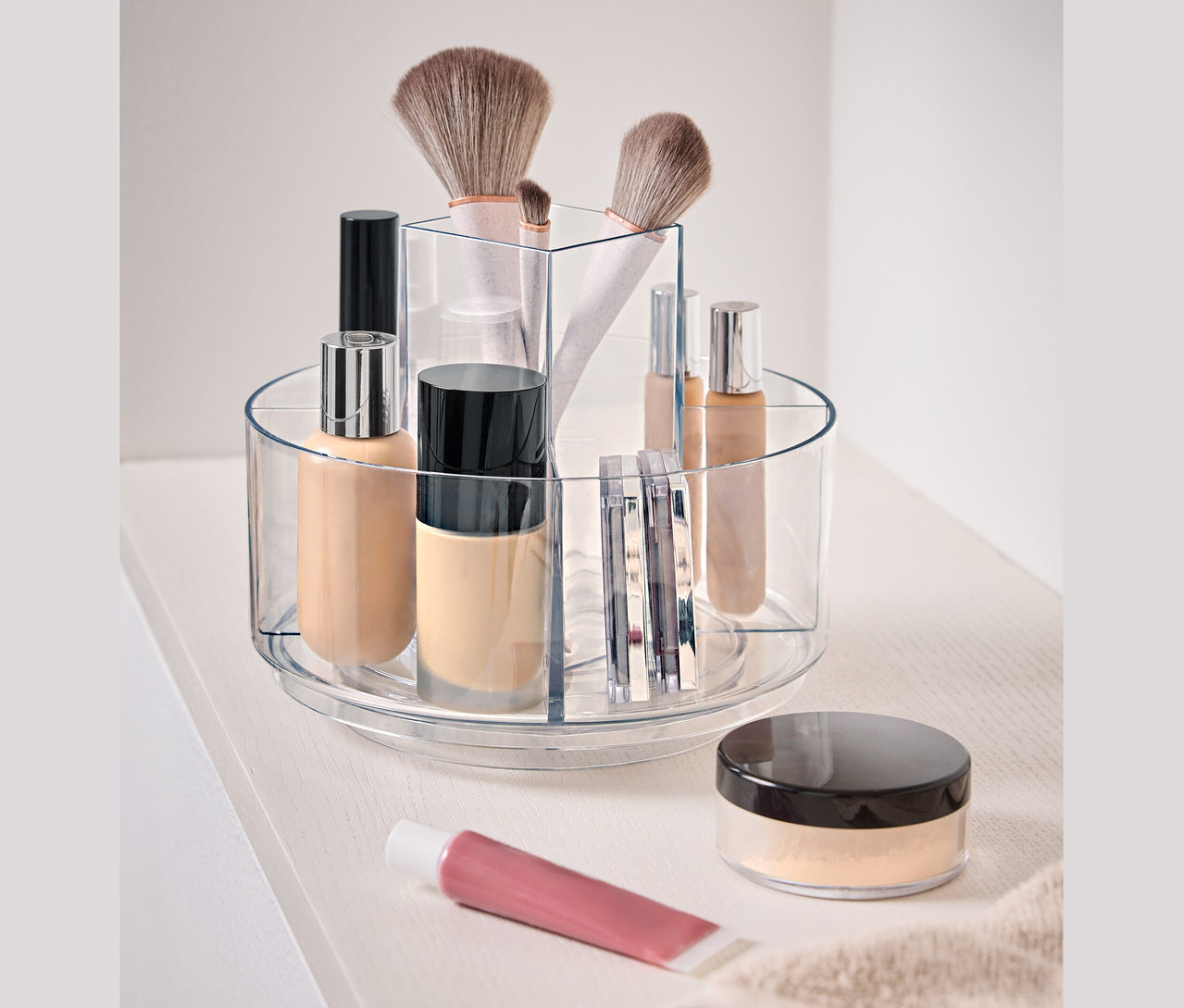 Récipient transparent rotatif contenant des cosmétiques sur une surface blanche.