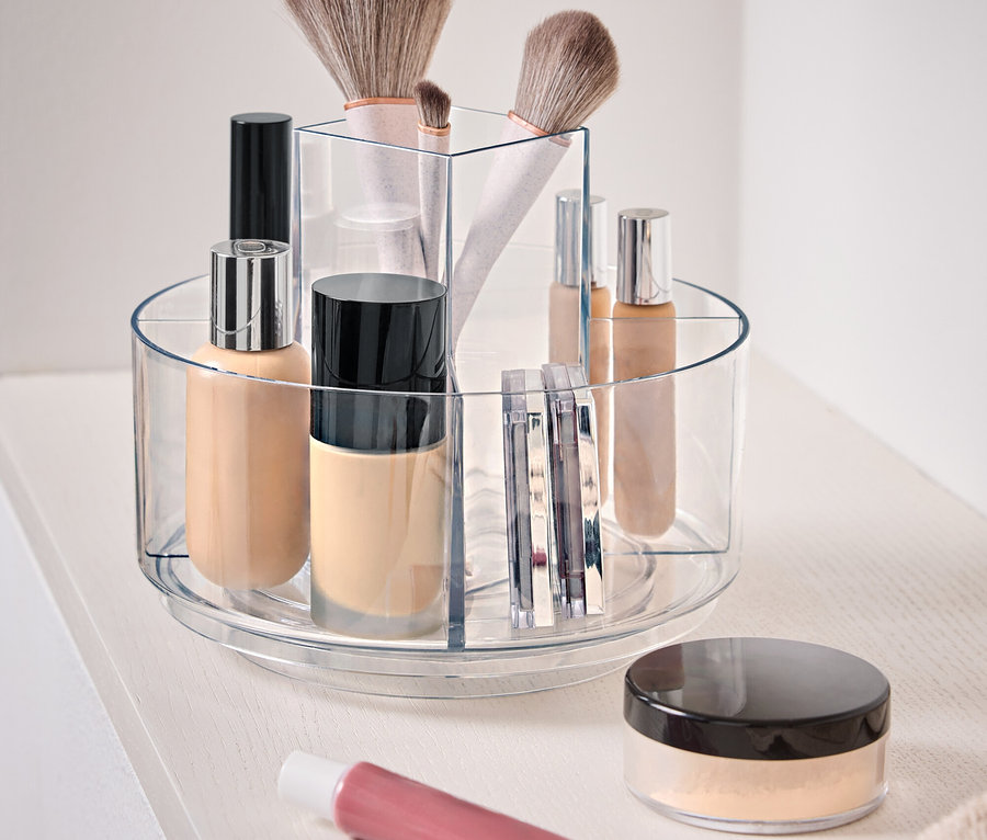 Récipient transparent rotatif contenant des cosmétiques sur une surface blanche.