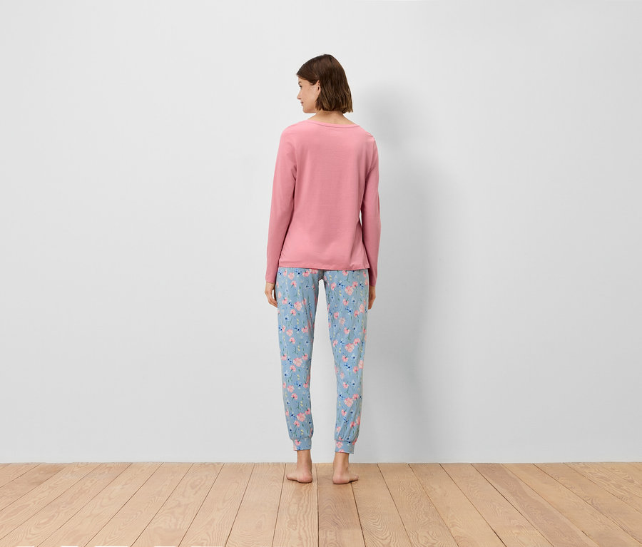 Une femme, de dos, porte un haut rose à manches longues et un pantalon bleu à motifs floraux.