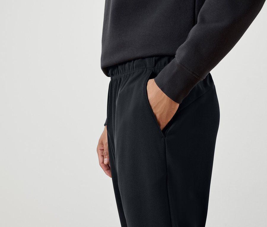 Un homme a la main dans la poche d'un pantalon de survêtement noir.