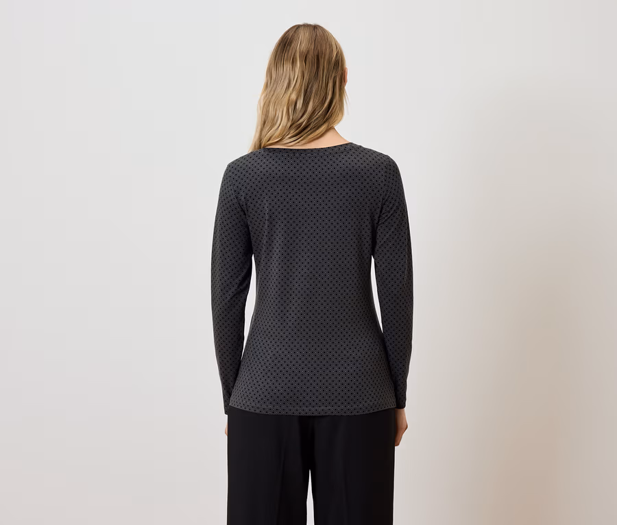 Une femme dos à la caméra porte un chemisier gris-noir à manches longues et un pantalon noir.