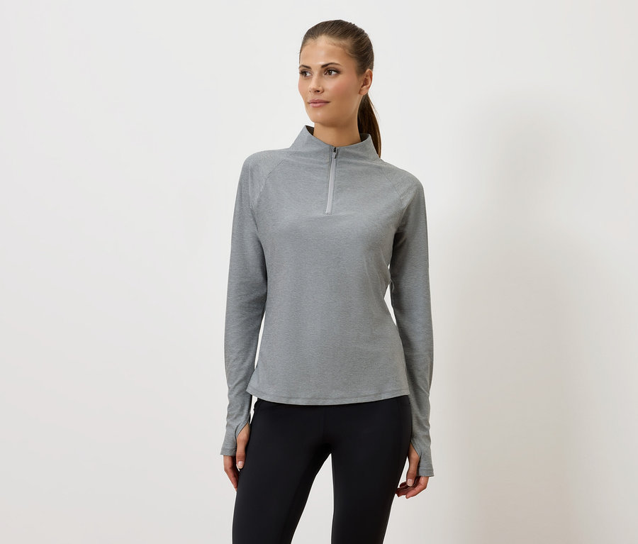 Femme portant un sweat-shirt gris à fermeture éclair et un legging noir, debout devant un fond blanc.