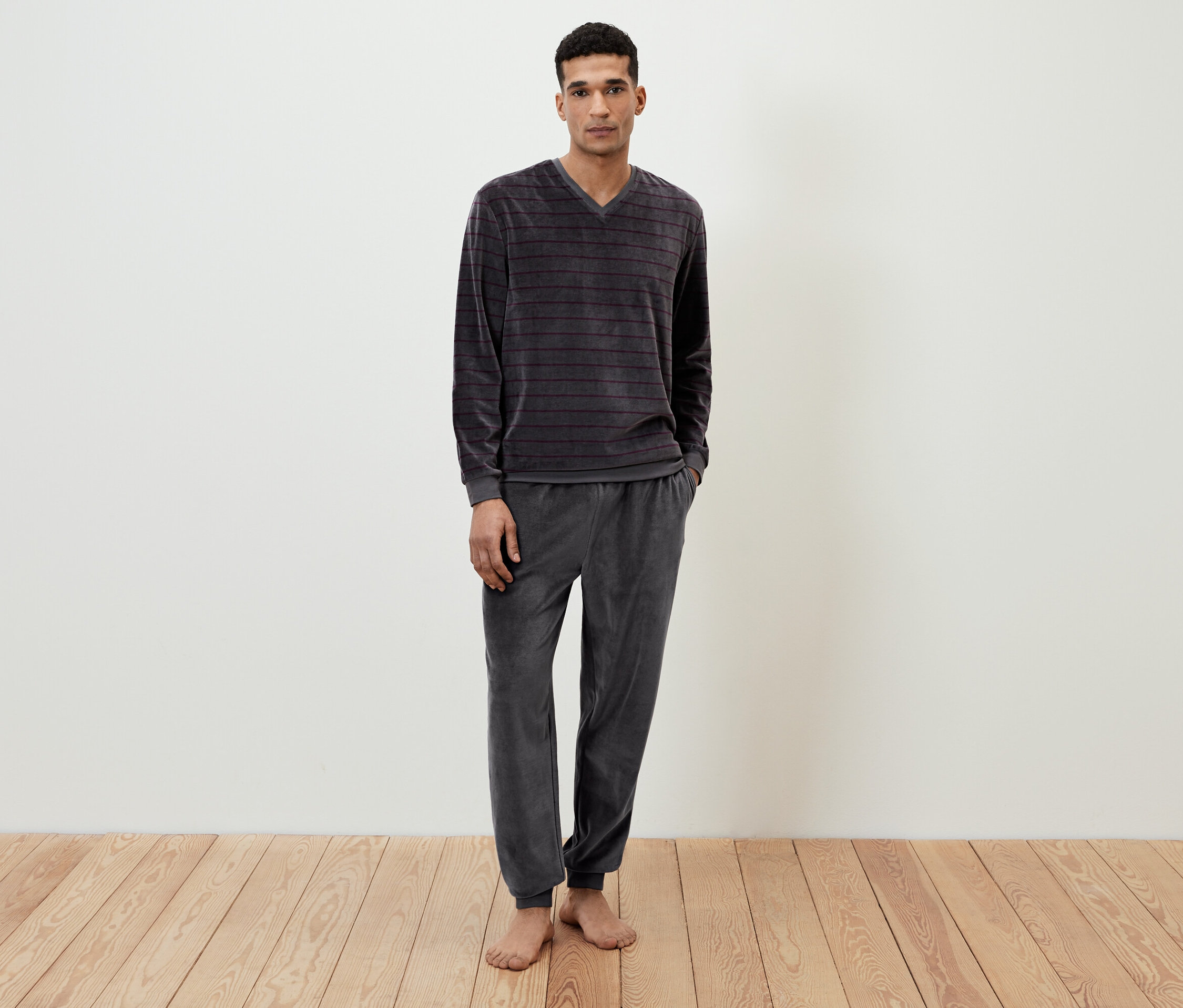 Un homme debout, pieds nus, portant un pyjama en velours gris rayé.