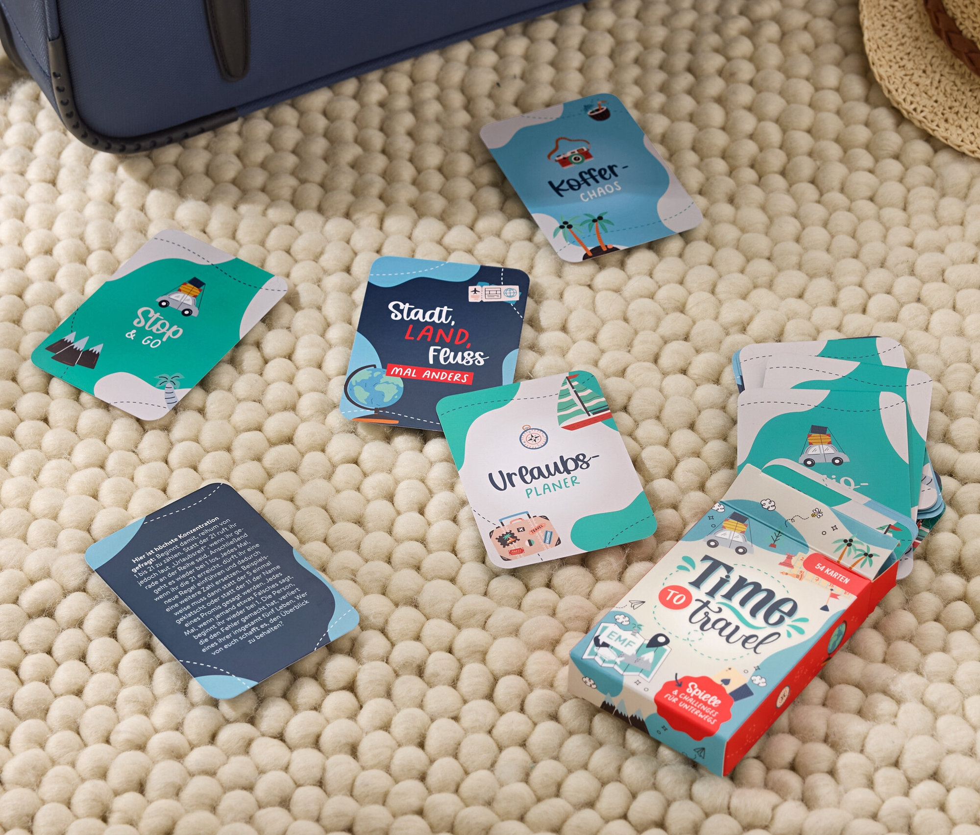 Sur un tapis beige se trouvent une valise, un chapeau et des cartes du set Time to Travel.