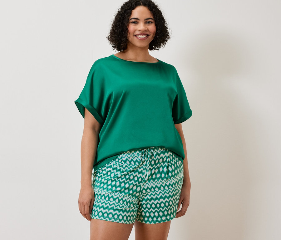 Une femme porte un chemisier turquoise bimatière et 2 shorts en jersey.