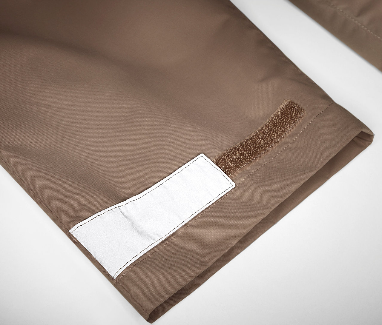 Détail d'un pantalon de pluie pour enfant avec réflecteur et fermeture velcro.