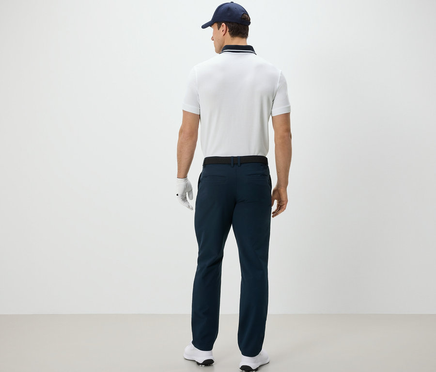 Un homme vu de dos porte un pantalon d’extérieur, un polo, une casquette et un gant de golf.