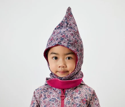 Portrait d'une petite fille aux yeux bruns portant une cagoule fleurie bordée de rose et une veste.