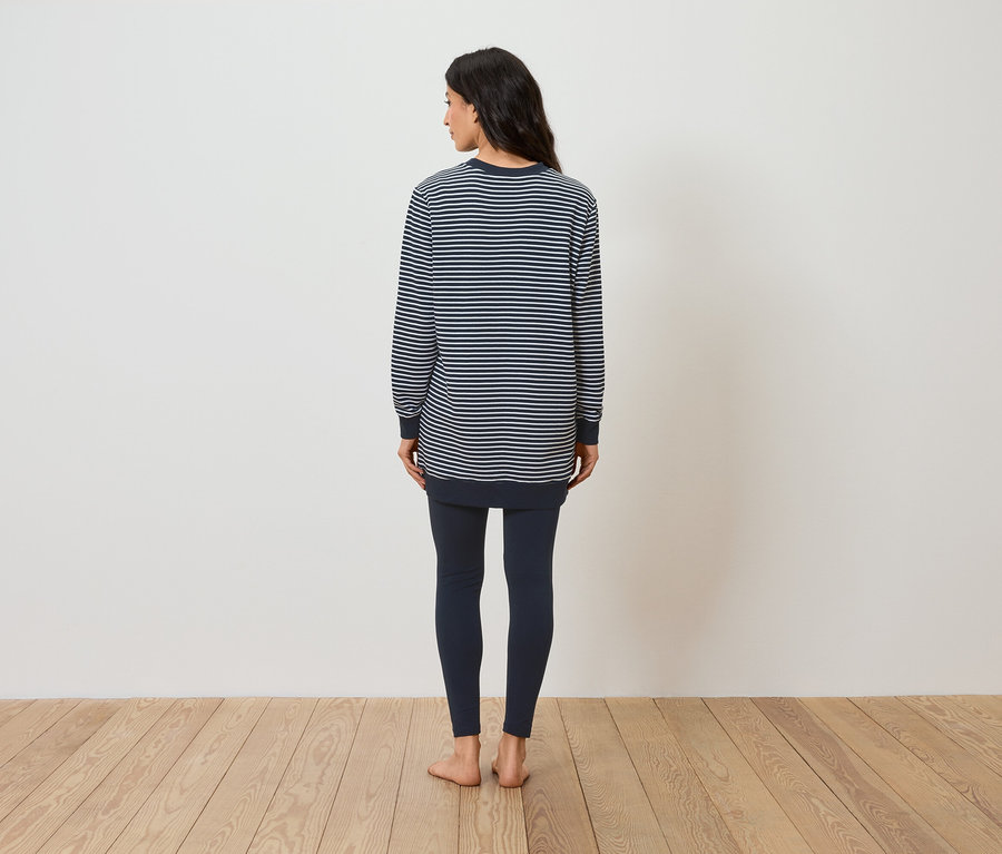 Une femme se tient dos à la caméra portant un haut rayé à manches longues et un legging.