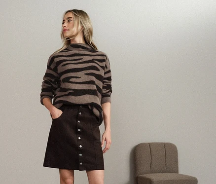 Femme portant une mini-jupe marron boutonnée et un pull rayé.
