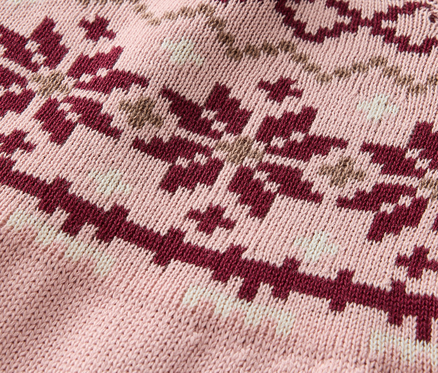 Gros plan d'un pull en tricot rose avec un motif de flocons de neige bordeaux et beige.