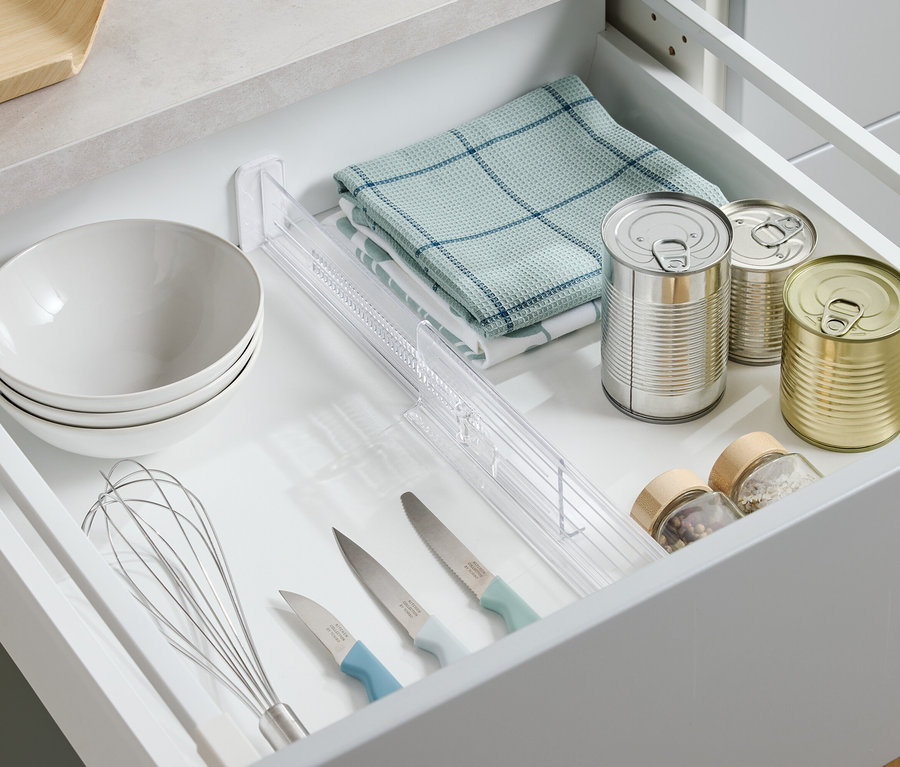 Vue de dessus d'un tiroir ouvert contenant des bols, un torchon, des boîtes de conserve, des épices, des couteaux et un fouet.