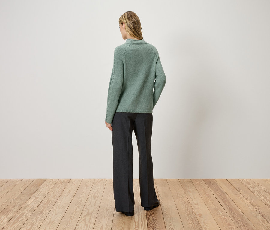 Une femme, de dos, porte un pull vert et un pantalon foncé.