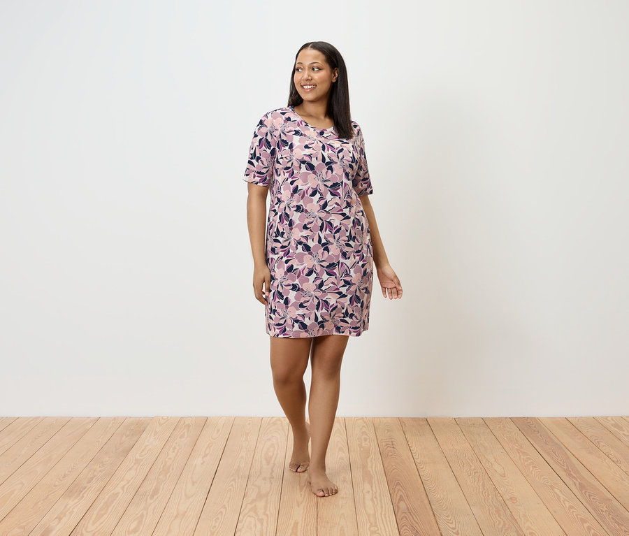 Une femme marche pieds nus sur un plancher en bois, portant une robe à fleurs.