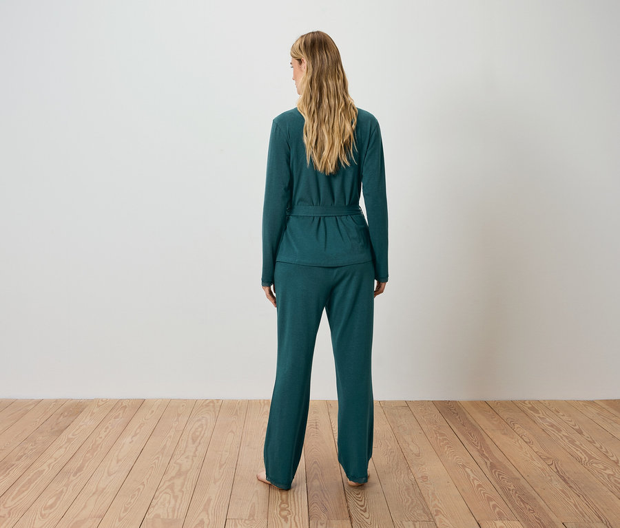 Une femme, vue de dos, porte un cardigan vert et un pantalon.